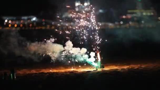 Pequeños fuegos artificiales blancos y verdes ardiendo y explotando en la playa — Vídeo de stock