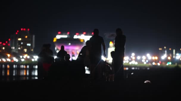 Jóvenes teniendo una fiesta en la playa por la noche en el fondo de los rascacielos brillantes y divertirse - fumar narguile — Vídeos de Stock