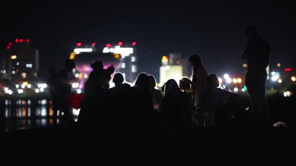 Jovens que fazem uma festa na praia à noite no fundo de arranha-céus - fumar narguilé e beber álcool — Vídeo de Stock