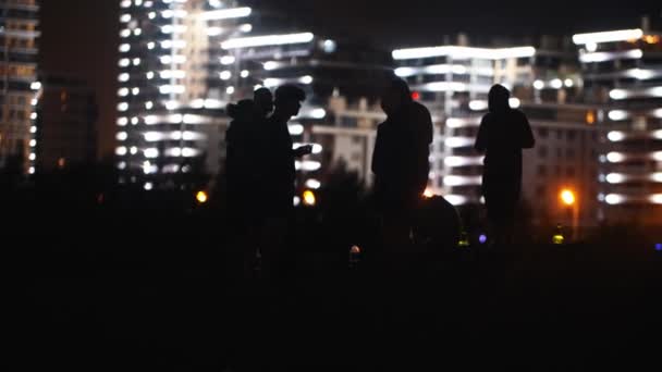 Młodzi ludzie urządzający imprezę na plaży w nocy na tle świecących nowoczesnych budynków - pijący alkohol — Wideo stockowe