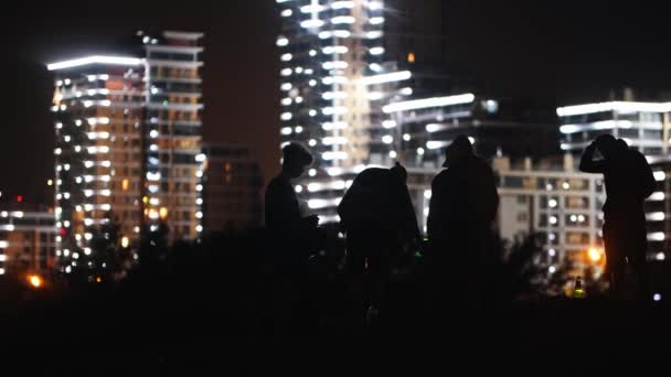 Les jeunes faisant une fête sur la plage la nuit sur le fond des bâtiments modernes lumineux fumer narguilé et boire de l'alcool — Video