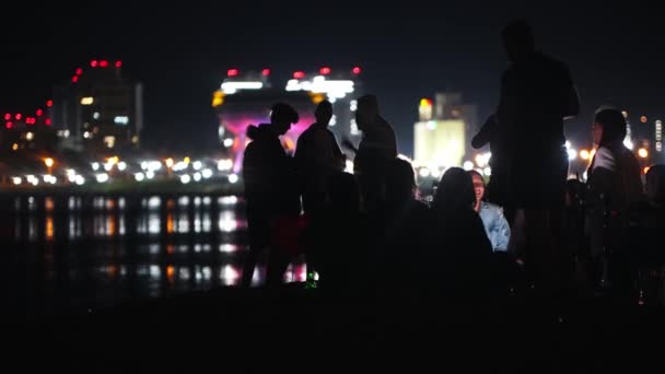Казань, Россия 16-06-2020: Молодые люди устраивают вечеринку на пляже ночью на фоне светящихся небоскребов - курение кальян и распитие алкоголя — стоковое видео