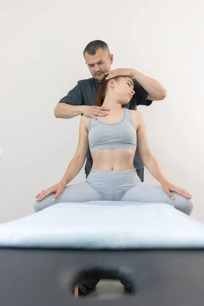 Chiropractische behandeling in de kliniek - jonge vrouw die op de bank zit - de arts die haar hoofd naar de zijkant draait — Stockfoto