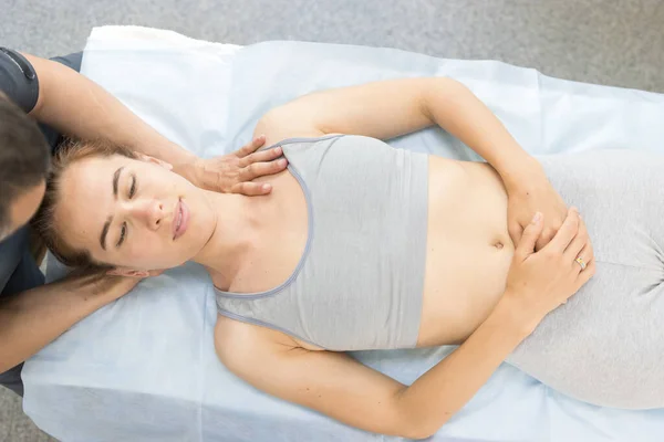 Mujer joven que recibe un tratamiento quiropráctico en la clínica, acostada en el sofá y el médico sosteniendo la cabeza y empujando el hombro — Foto de Stock