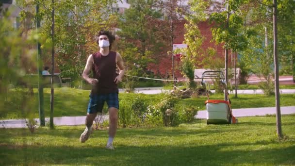 Un giovane uomo in maschera medica corre nel parco e inizia a scaldarsi — Video Stock