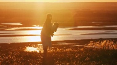 Gün batımında kızıyla tepede oynayan genç bir kadın.