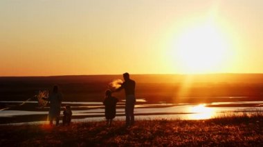 Genç bir aile sahada uçurtmayla oynarken parlak turuncu gün batımı