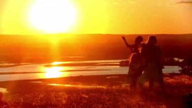 Genç bir aile sahada oynarken parlak turuncu gün batımı ve uçurtma uçururken