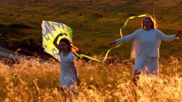 Jonge moeder met haar dochter rennen op de heuvel met de vlieger bij zonsondergang — Stockvideo