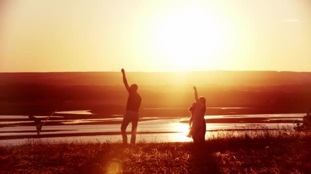 Ung familj leker på planen medan den ljusa orange solnedgången - far håller draken — Stockvideo