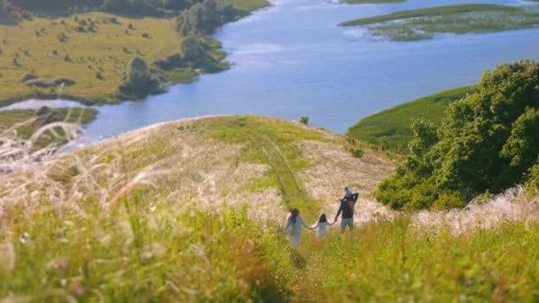 Mladá šťastná rodina kráčí dolů z kopce k řece — Stock video