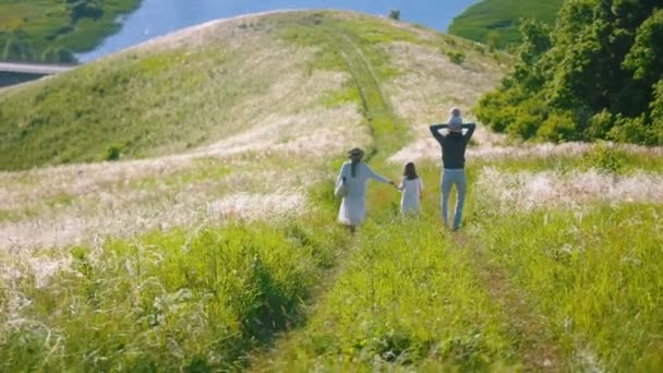 Ung lycklig familj promenader på gräsbevuxen stig ner för backen — Stockvideo