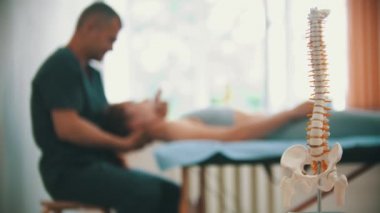 Klinikte osteopatik tedavi gören bir kadın. Ön planda insan omurgasının plastik bir örneği.