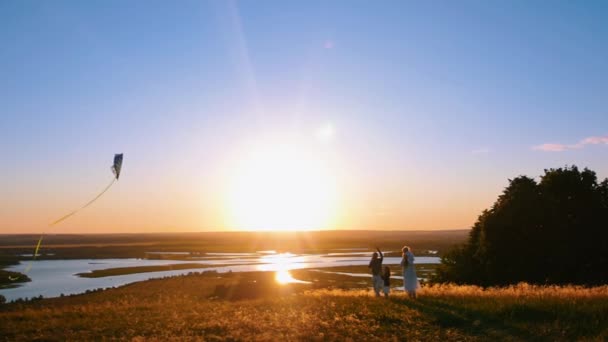 Junge vierköpfige Familie spielt an einem frühen Sonnenuntergang mit einem Drachen auf dem Feld — Stockvideo