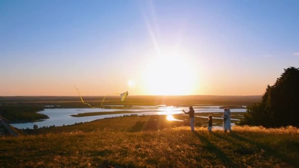 Młoda czteroosobowa rodzina bawi się latawcem na wzgórzu o wczesnym zachodzie słońca — Wideo stockowe
