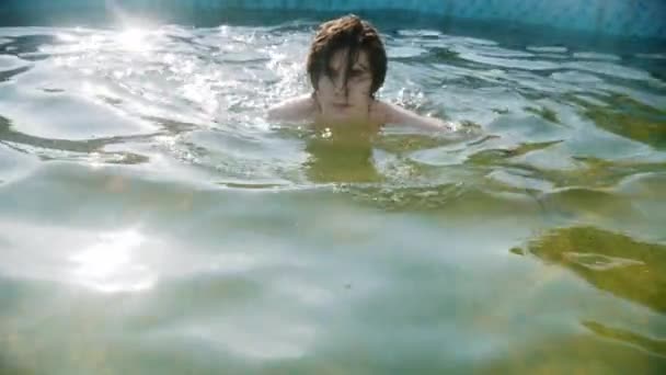 Genç adam havuzda yüzüyor ve kameraya bakıyor. — Stok video