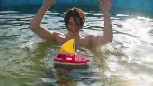 Młody człowiek bawiący się łódką w basenie — Wideo stockowe