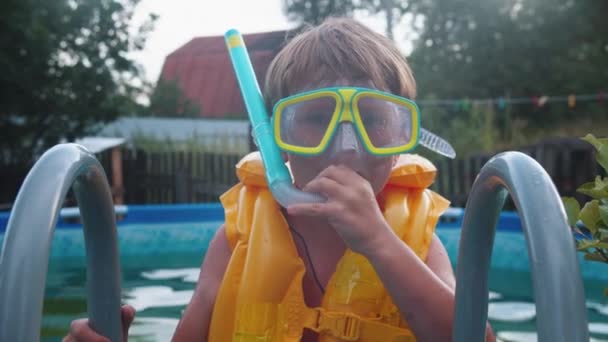 Sualtı maskeli küçük bir çocuk şişme havuzda yüzüyor ve ağzına bir tüp sokuyor. — Stok video