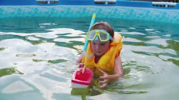 Ein kleiner Junge in Unterwassermaske spielt mit einem Spielzeugboot im Schwimmbad — Stockvideo