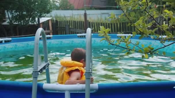 En liten pojke som simmar i den uppblåsbara poolen utomhus — Stockvideo