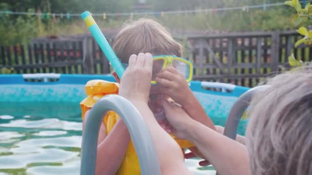 Malý chlapec v podvodní masce, který se chystá plavat v nafukovacím bazénu - jeho babička mu pomáhá strkat trubičku do pusy — Stock video