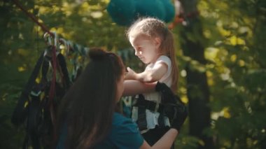 Kadın eğitmen, küçük bir kıza yardım ediyor. İp macerası için sigorta kemerini takıyor.