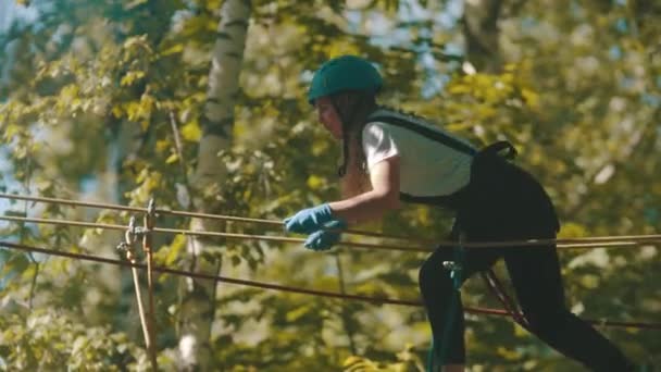 Eine Frau mit Helm überquert die Hängebrücke - eine Attraktion im Wald — Stockvideo