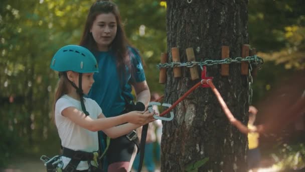Woman instructor explaining to a little girl how to use an insurance hook attached to the rope - the girl using it — Stock Video
