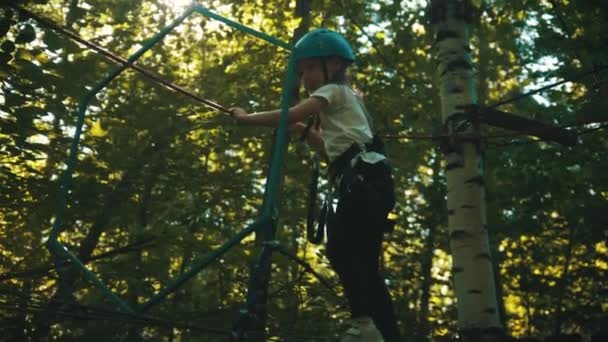 Ein kleines Mädchen, das auf der Seilbrücke geht und sich an den Seilen festhält — Stockvideo