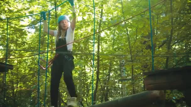 Jovem em uma atração no parque - andando sobre os troncos pendurados em cordas para o estande e sua filha — Vídeo de Stock