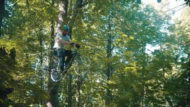 Een man die de touwen oversteekt tussen twee bomen op de fiets. — Stockvideo