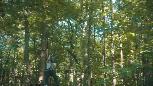 Человек, имеющий веревку приключения в лесу с полной страховкой - спускаясь к стенду с помощью своего страхового пояса — стоковое видео