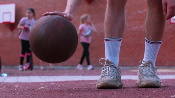 Młody człowiek na boisku do koszykówki uderza piłkę — Wideo stockowe