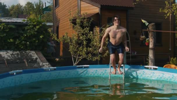 Młody człowiek skacze do nadmuchiwanego basenu w pobliżu swojego domu na wsi — Wideo stockowe