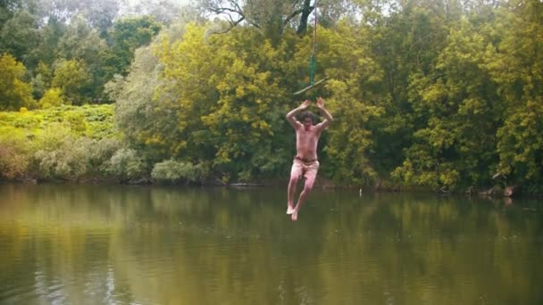 Mladý muž letící nad vodou a držící se u baru - padající do vody — Stock video