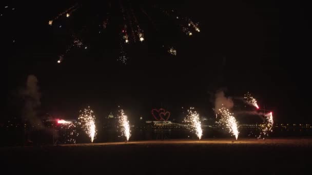 Robbanó és forgó tűzijáték a tengerparton, és égő állni a szív alakja — Stock videók