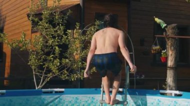 Arkadan şişme havuza atlayan genç adam.