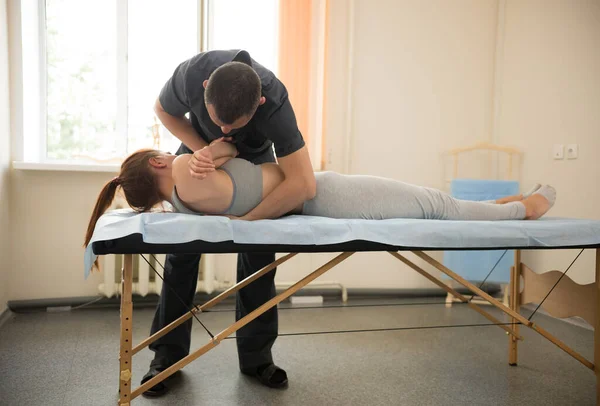 Молодая женщина, проходящая лечение остеопатии в помещении - женщина лежит на боку и мастер делает упражнения — стоковое фото