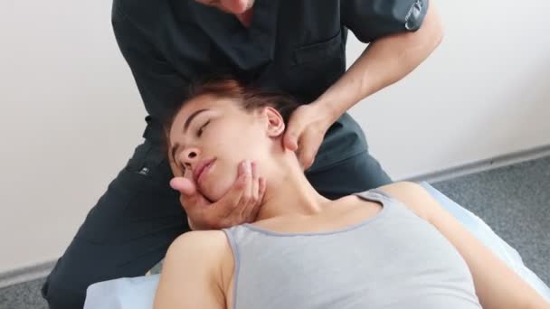Massagista segurando pescoço de mulheres jovens virou-se para o lado enquanto ela está deitada em um sofá redução de vértebras — Vídeo de Stock