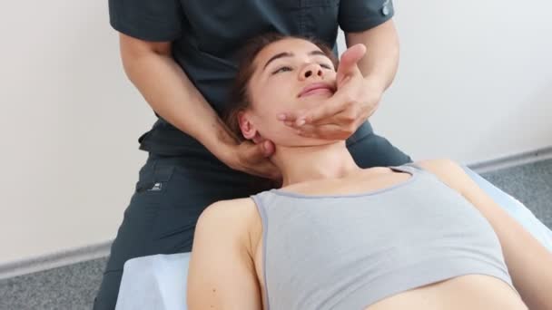 Massagista trabalhando com o pescoço de mulheres jovens e empurrando em seus ombros enquanto ela está deitada em um sofá — Vídeo de Stock