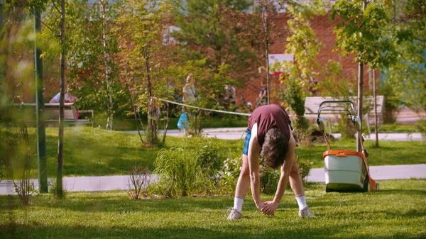 En ung man värmer upp i den gröna parken - böjer sig ner — Stockfoto