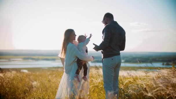 Joven familia feliz con el pequeño bebé de pie en el campo — Vídeos de Stock