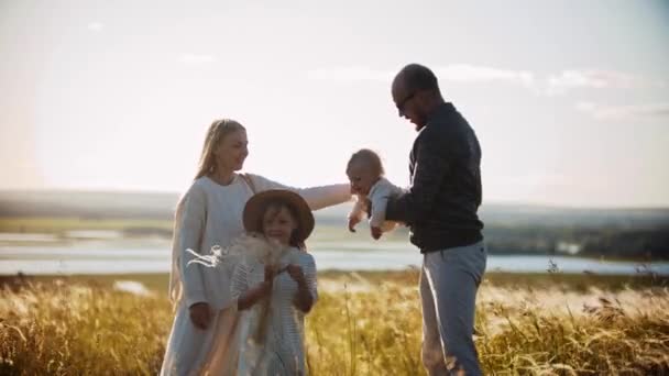 Ung familj står på vetefältet - far håller ett litet barn på händerna och liten flicka står nära sin mor — Stockvideo