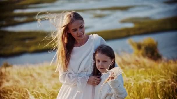 Young smiling woman hugging her daughter standing on the wheat field - girl waving her hand with the wheat — Stock Video