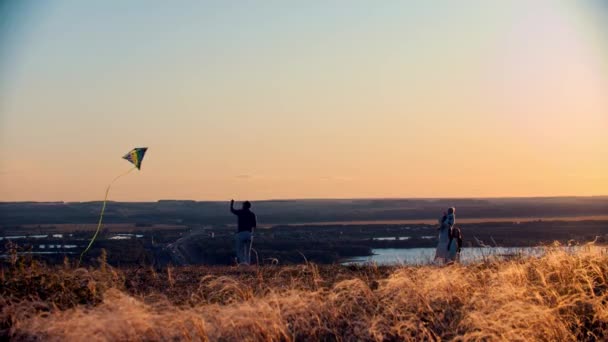 Junge Familie spielt bei Sonnenuntergang mit Drachen auf dem Feld - Vater führt Drachen — Stockvideo