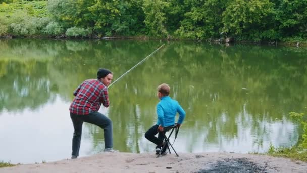 Balık tutan iki kardeş, oltayı çeken bir adam ve onu izleyen küçük kardeşi. — Stok video