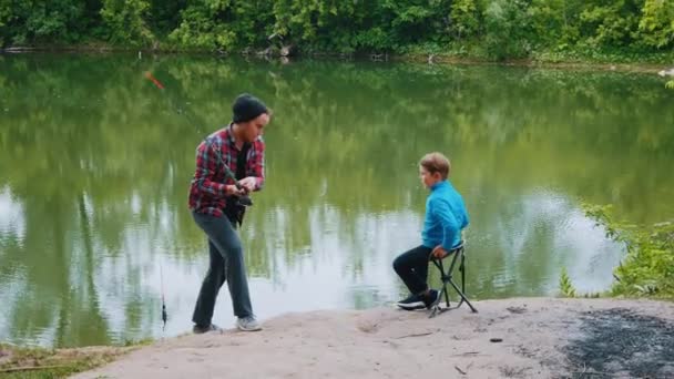 Dos hermanos en la pesca - un hombre lanza una caña de pescar en el agua — Vídeo de stock