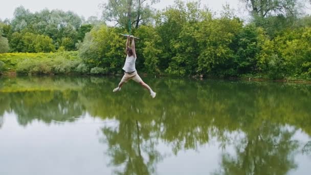 Young man flying above the water holding by the wooden bar — Stock Video