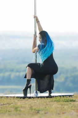 Yüksek topuklu mavi örgülü bir kadın direğin yanında dans ediyor.