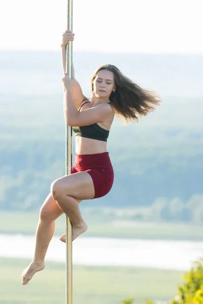 Young woman in sports clothes holding by the pole and spinning on it